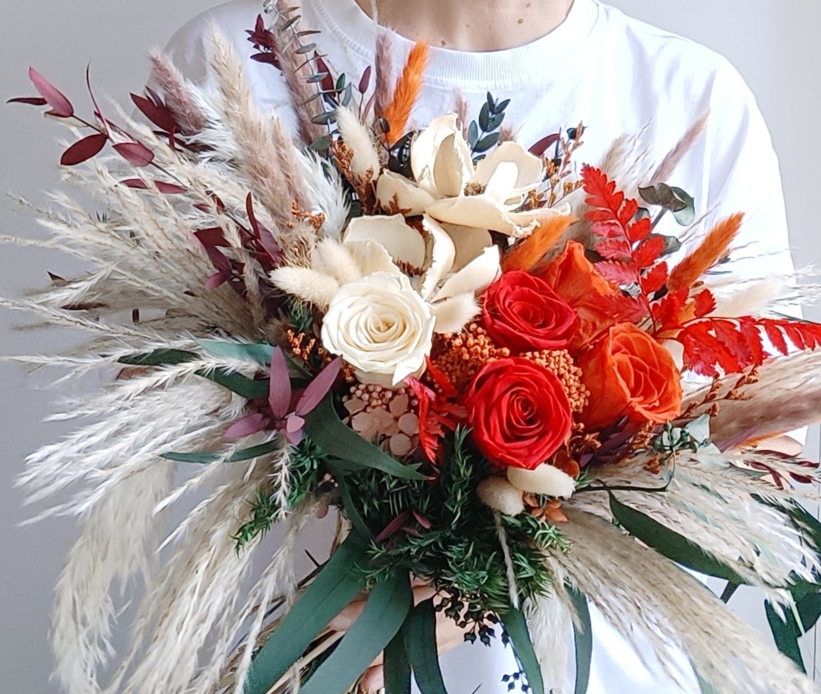 Detailed close-up of bridal bouquet with preserved red and white roses, natural pampas grass, and mixed dried foliage for a rustic boho wedding