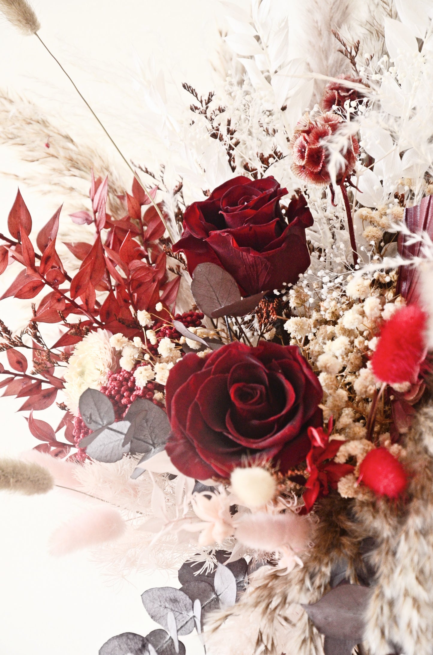 Side view of boho rustic bridal bouquet with burgundy roses, beige pampas grass and preserved eucalyptus, dried wedding flowers.