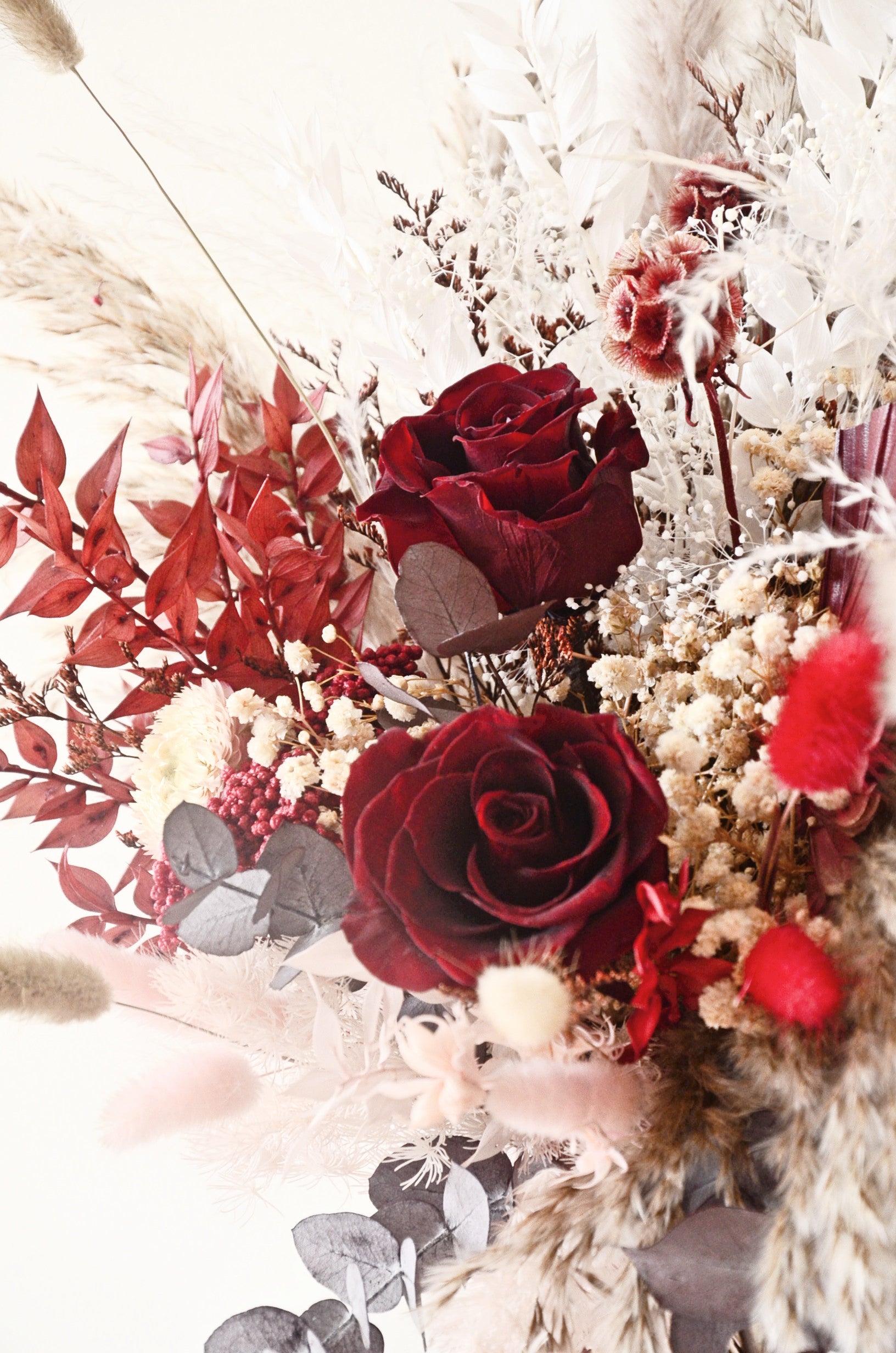 Side view of boho rustic bridal bouquet with burgundy roses, beige pampas grass and preserved eucalyptus, dried wedding flowers.