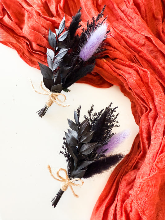 Boho wedding boutonniere featuring black foliage, preserved flowers, and soft lavender accents, styled with natural twine ribbon.