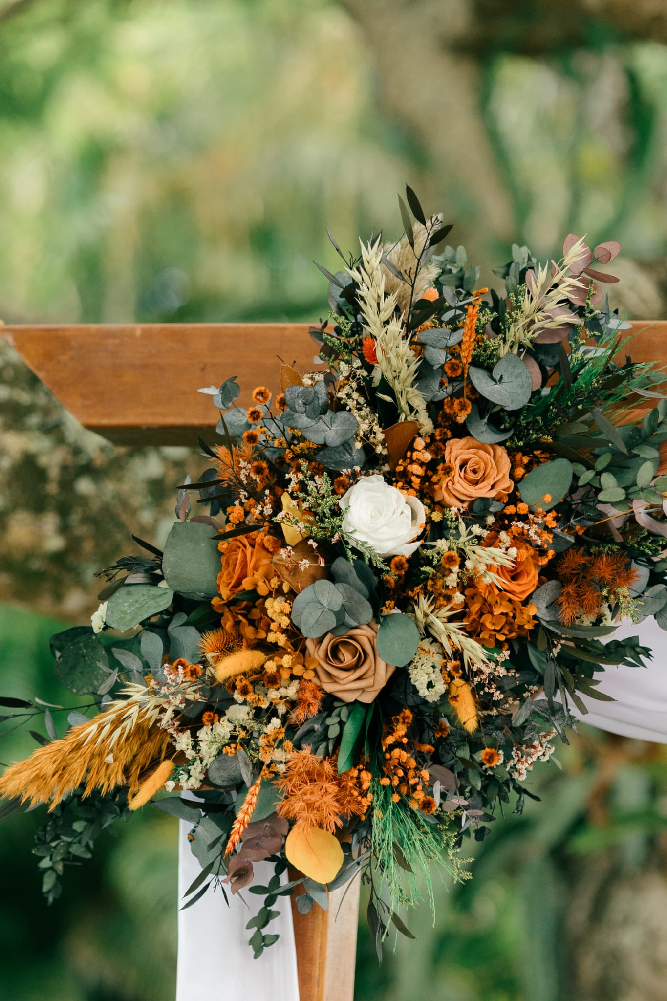 Rustic outdoor wedding arch with boho dried flower arrangements and soft draped fabric in a natural garden setting