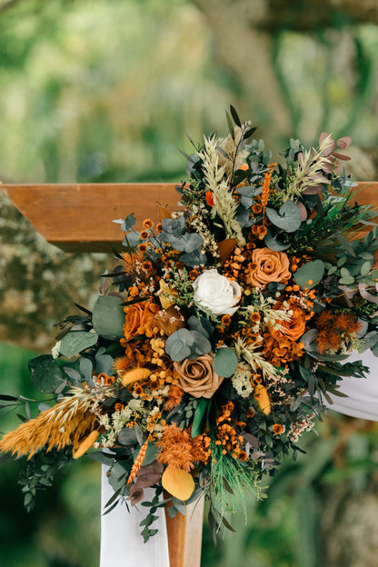 Rustic outdoor wedding arch with boho dried flower arrangements and soft draped fabric in a natural garden setting