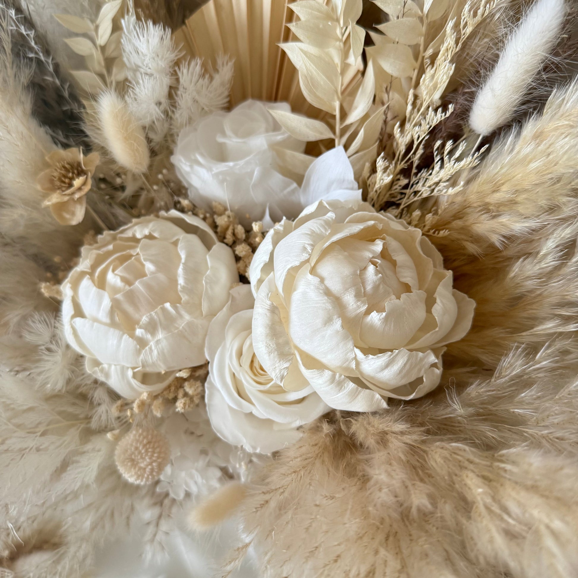 Close-up of a floral peony bridal bouquet with white flowers and dried foliage on a neutral background