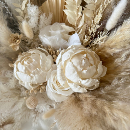 Close-up of a floral peony bridal bouquet with white flowers and dried foliage on a neutral background