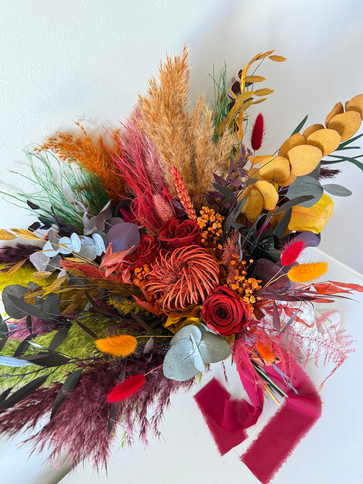 A vibrant dried flower bouquet featuring a mix of autumn and winter colors including red, orange, yellow, green, and purple elements, arranged on