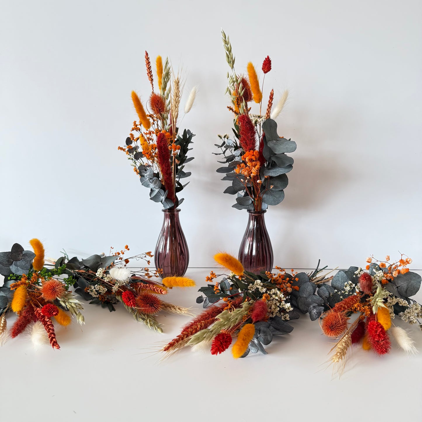 Two brown vases with dried floral arrangements on a white background