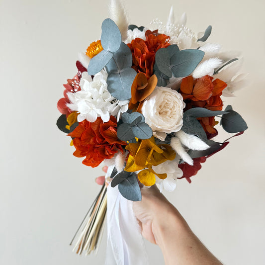 HANDCRAFTED dried and preserved bridal bouquet featuring terracotta, burnt orange, and mustard flowers with eucalyptus leaves for a boho autumn wedding