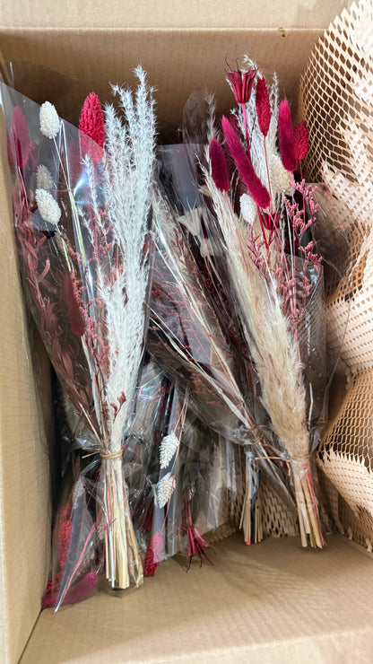 Several small dried flower bouquets wrapped in clear plastic inside a cardboard box. The bouquets feature white, pink, and burgundy dried flowers with beige grasses.