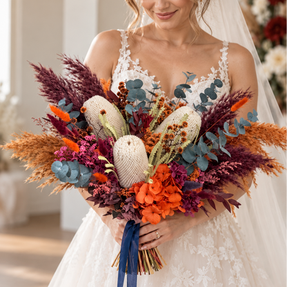 Bride holding a colourful Australian native bridal bouquet with banksia, orange dried flowers, burgundy foliage and blue eucalyptus.
 