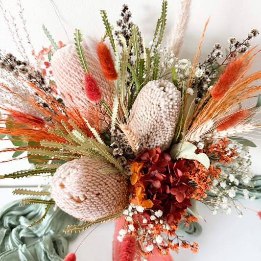 Natural bridal bouquet set featuring dried banksia and wildflowers in autumn colours, styled with green fabric