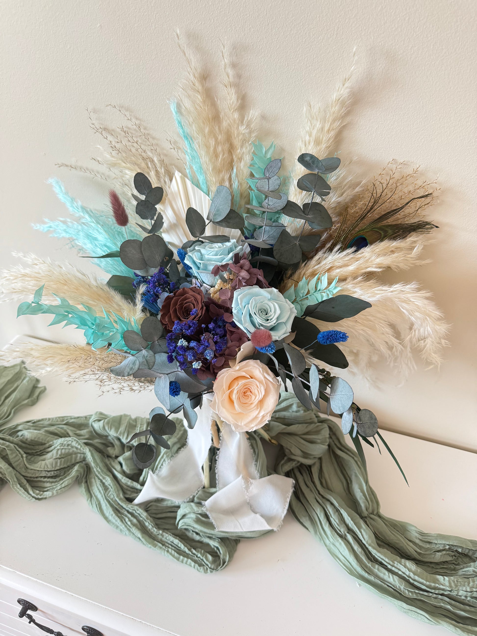 Boho wedding bouquet in teal, navy and beige tones with fluffy grass and preserved foliage.