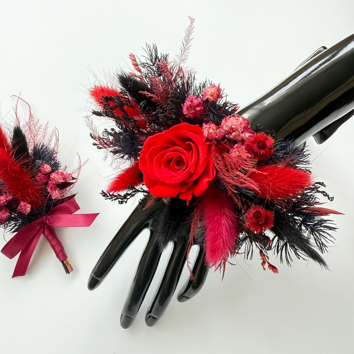 Red dried rose corsage with black foliage and matching boutonniere presented together for prom or wedding.