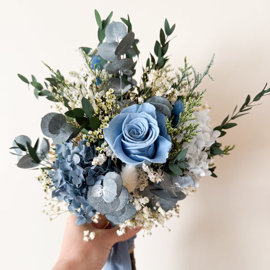 Blue and white dried flower bridal bouquet tied with soft blue ribbon, featuring rustic natural textures for weddings.