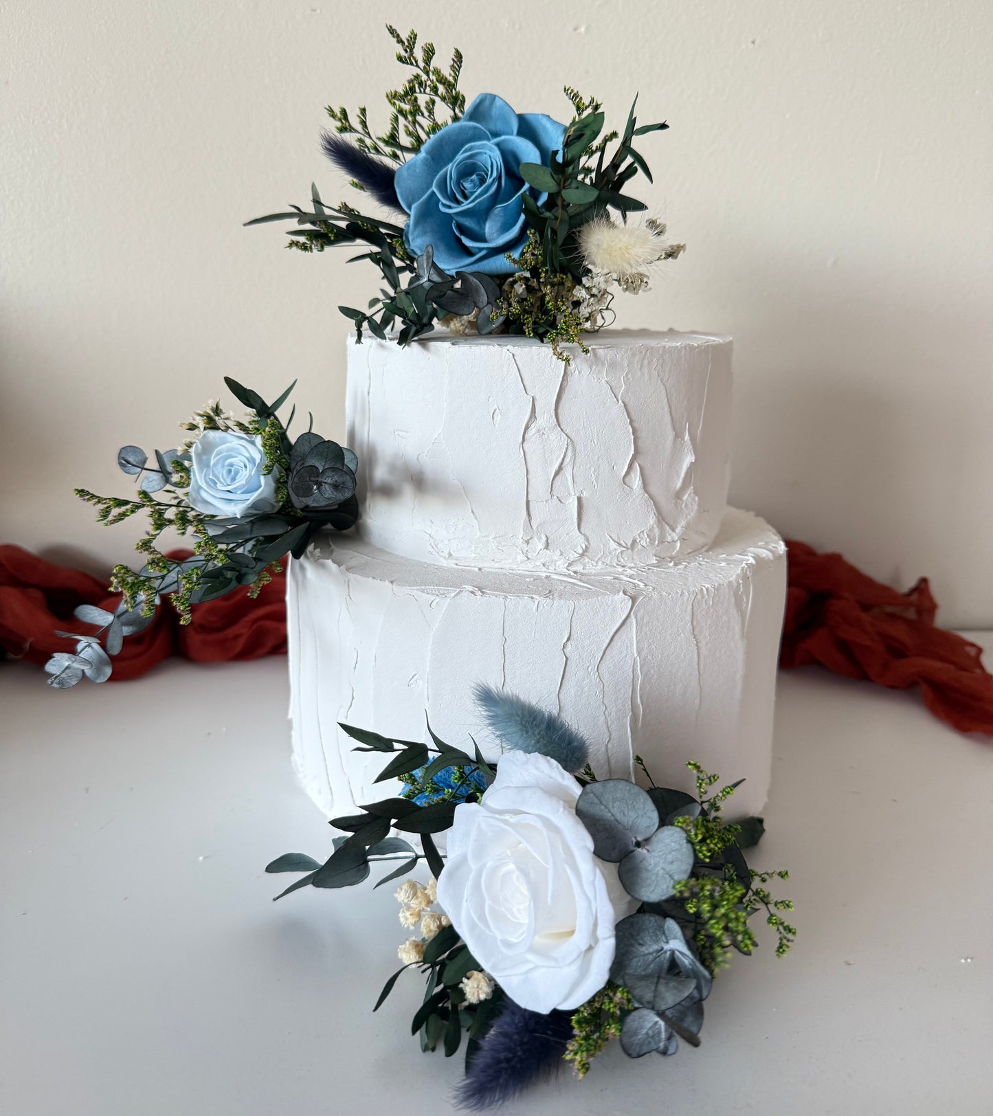 Wedding cake decorated with matching blue dried flower arrangements, including roses, babyâ€™s breath and greenery