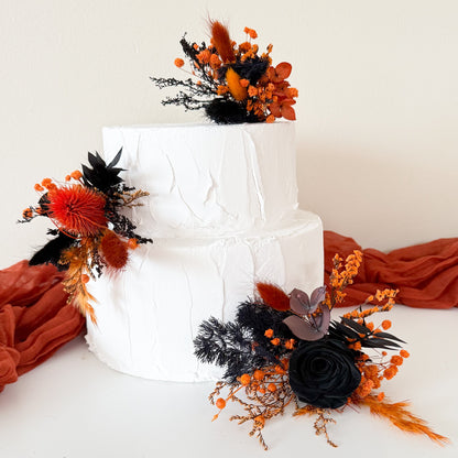 Two-tier white cake decorated with gothic black and burnt orange dried flowers in boho style