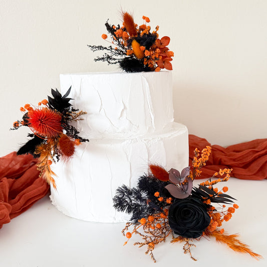 Two-tier white cake decorated with gothic black and burnt orange dried flowers in boho style