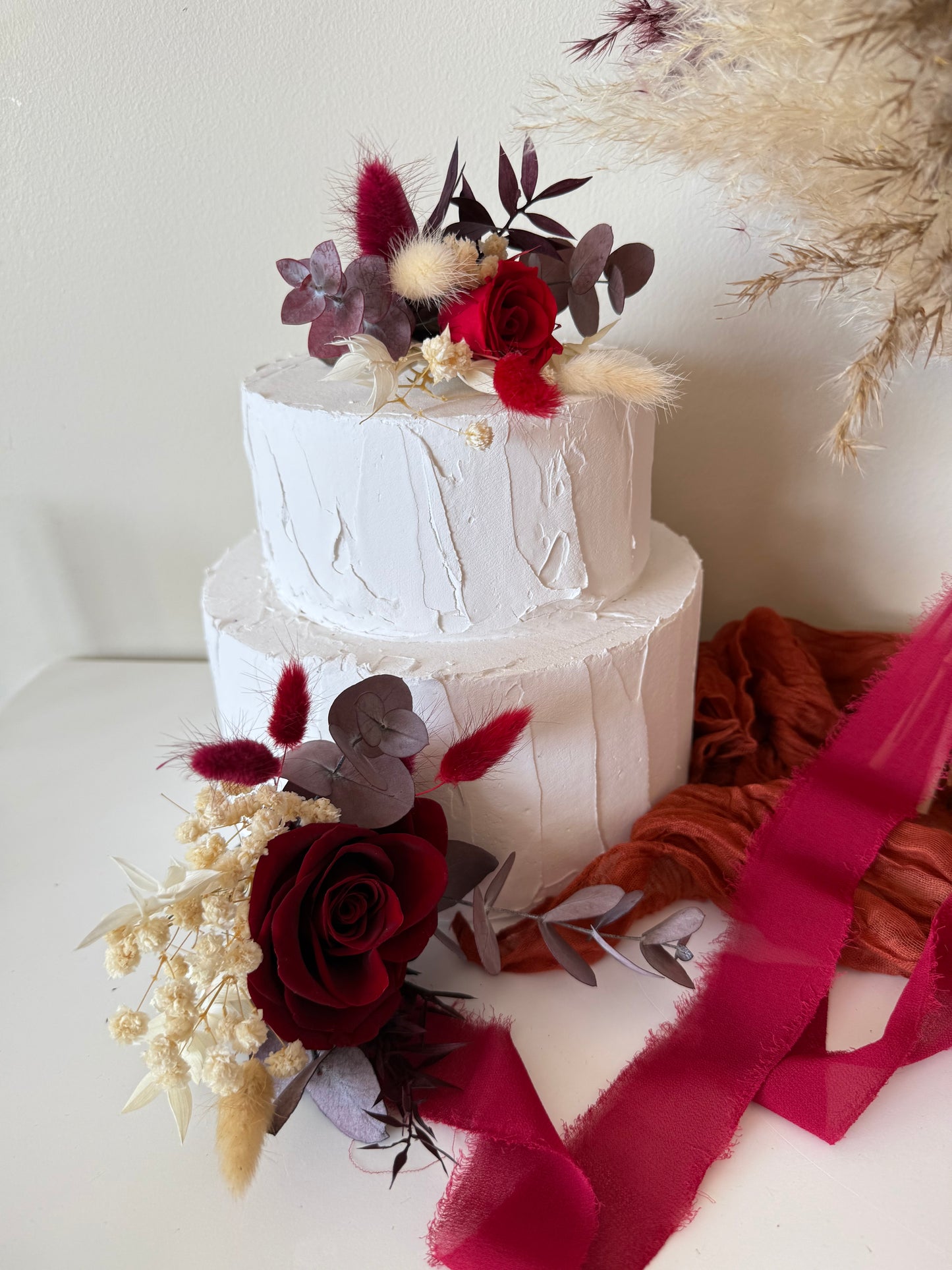 Elegant wedding cake decorated with burgundy roses, ivory dried blooms and preserved foliage