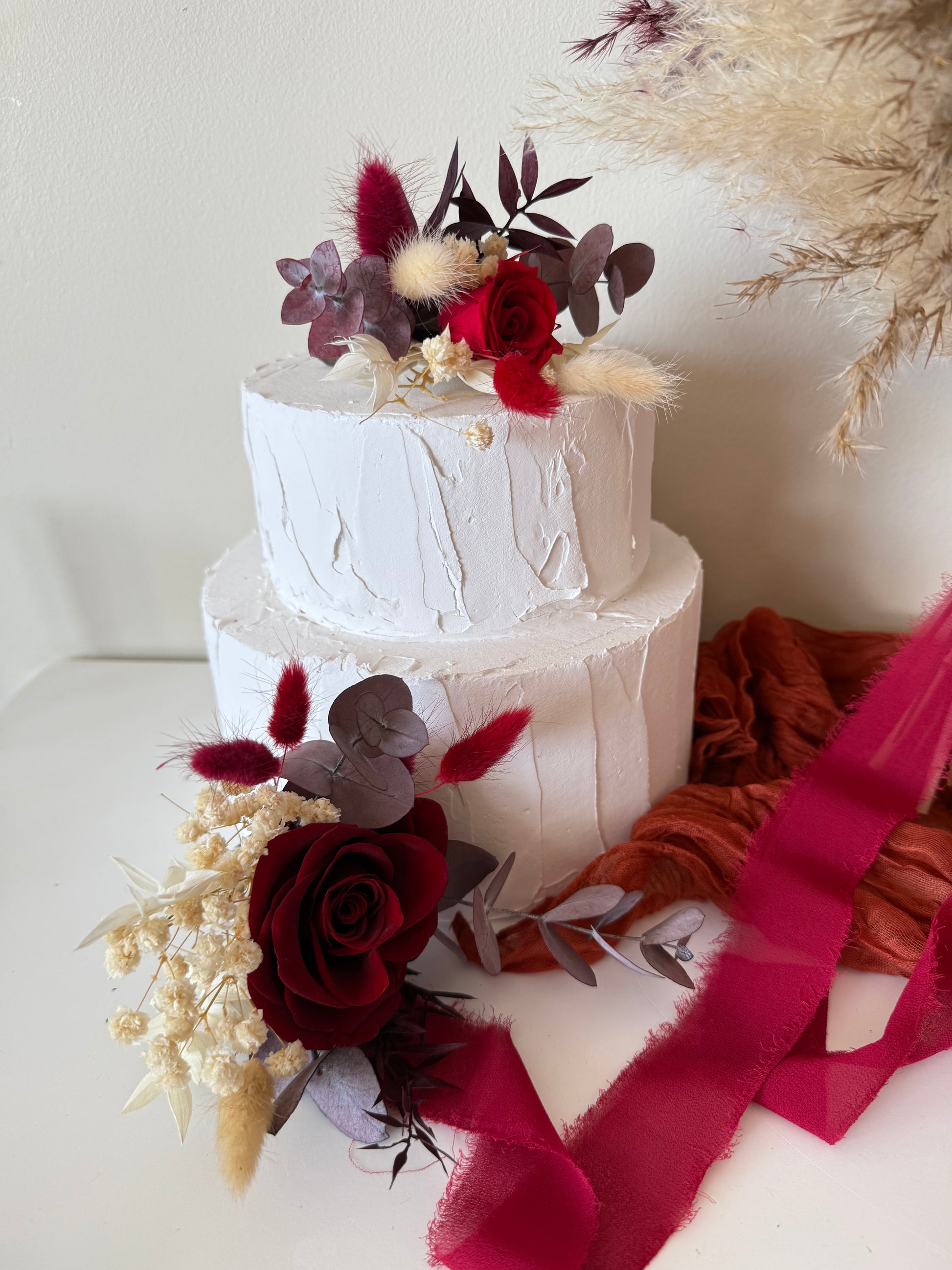 Elegant wedding cake decorated with burgundy roses, ivory dried blooms and preserved foliage