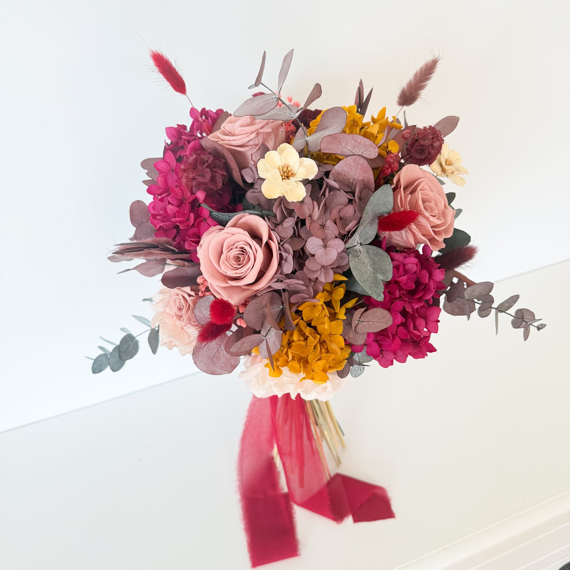 Boho bridal bouquet made with burgundy, dusty pink, and mustard dried flowers, tied with red silk ribbon, perfect for rustic Australian weddings