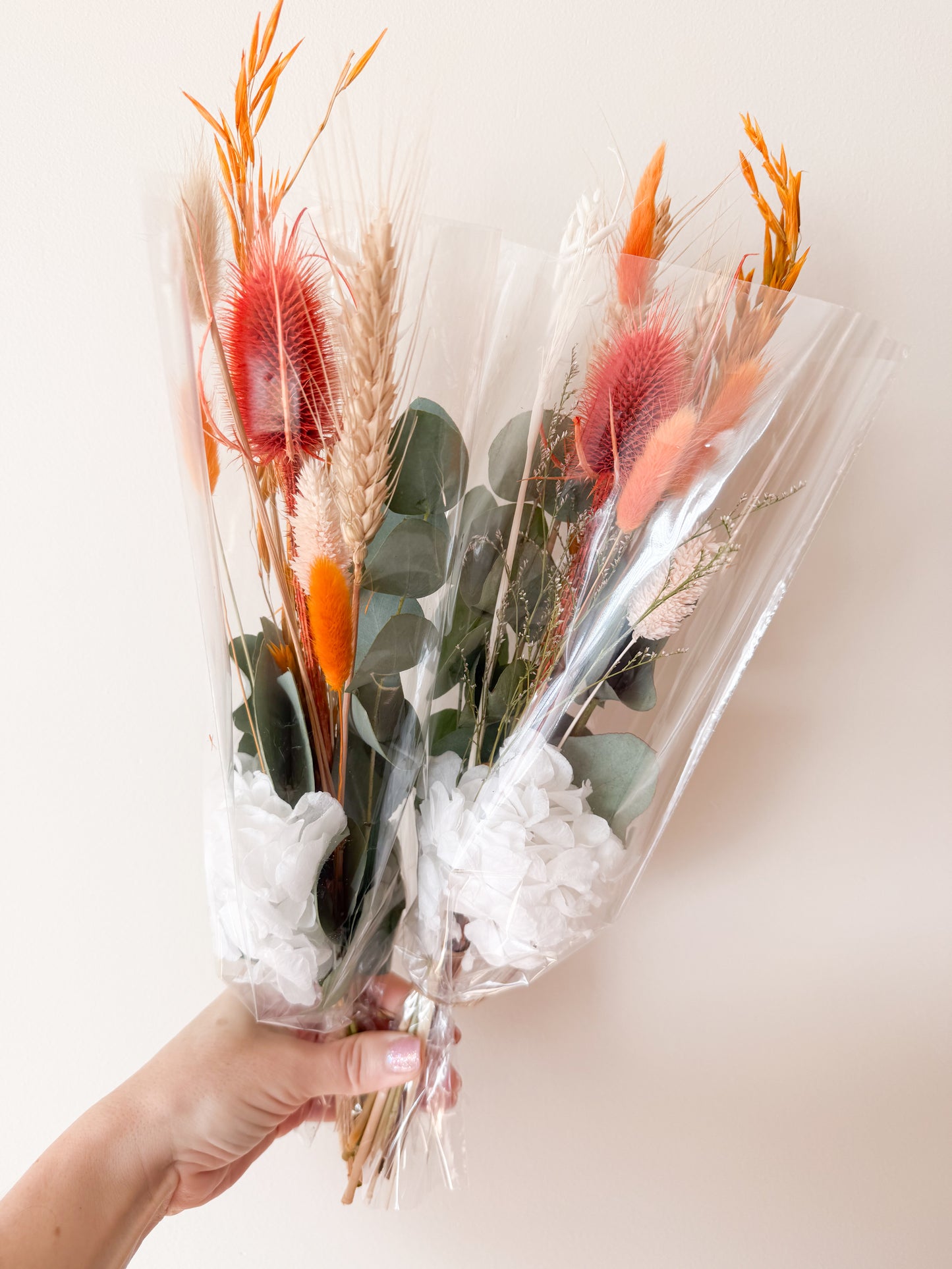 Bouquet of dried flowers and greenery in clear cellophane wrap held by a hand against a light background
