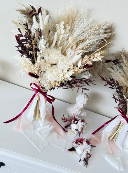Bouquet of dried flowers with a burgundy ribbon on a white surface
