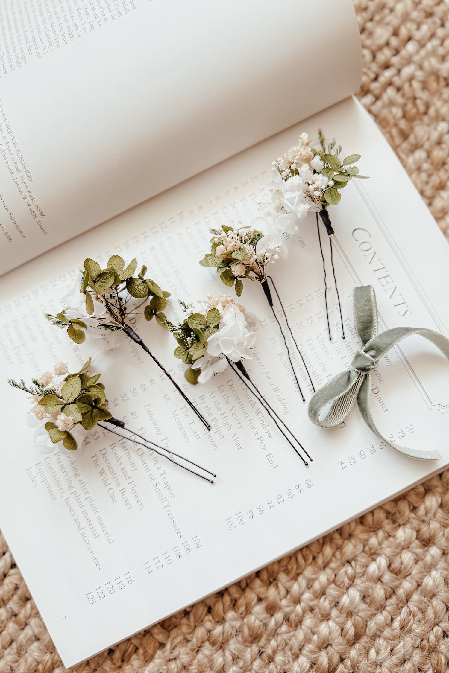 Flatlay of white dried flower bridal hair pins displayed on an open book, ideal for elegant boho and rustic wedding looks