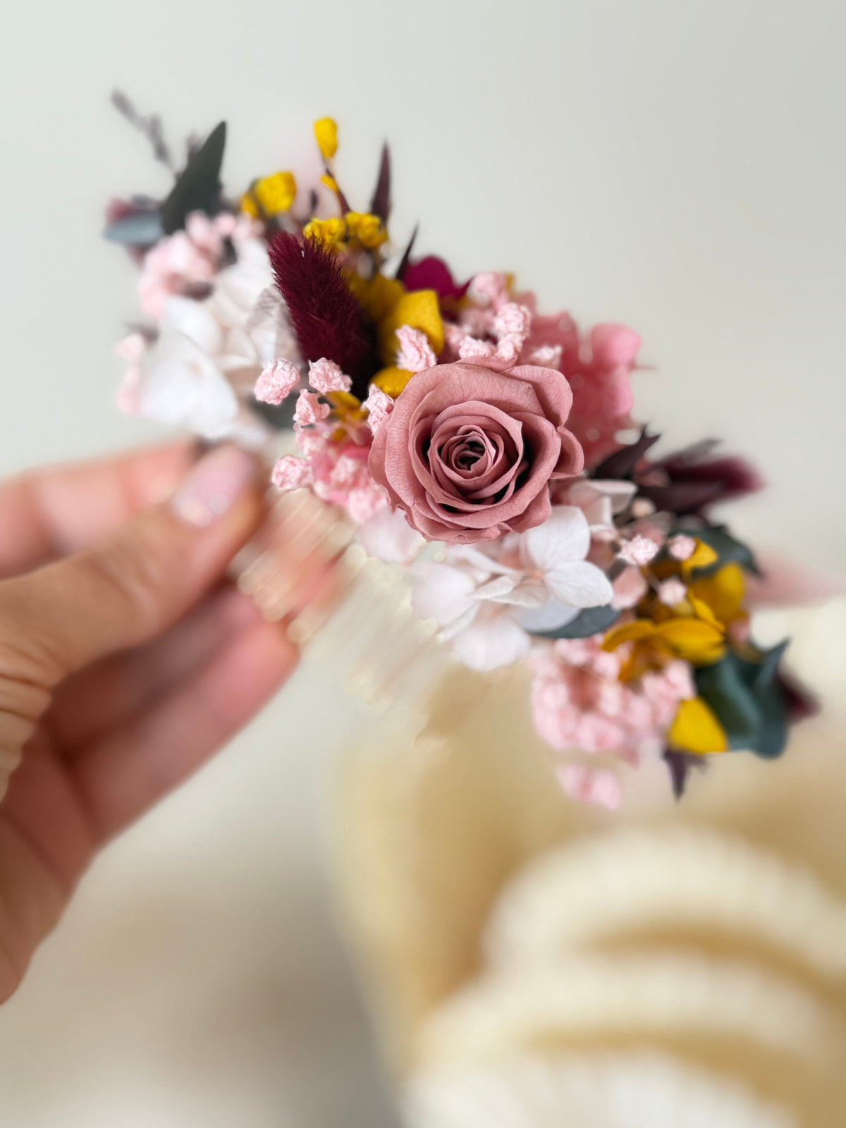 Floral headband with pink and yellow flowers held by a hand against a blurred background