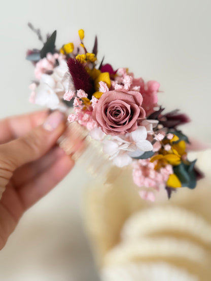 Floral headband with pink and yellow flowers held by a hand against a blurred background