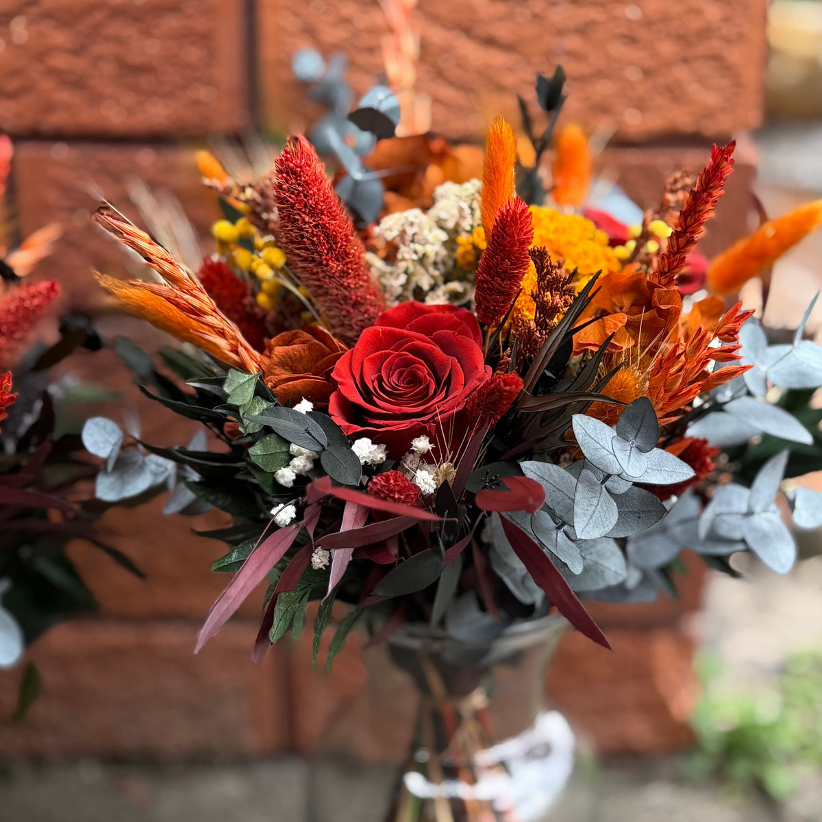 Bouquet of red and orange flowers in a glass vase against a brick wall