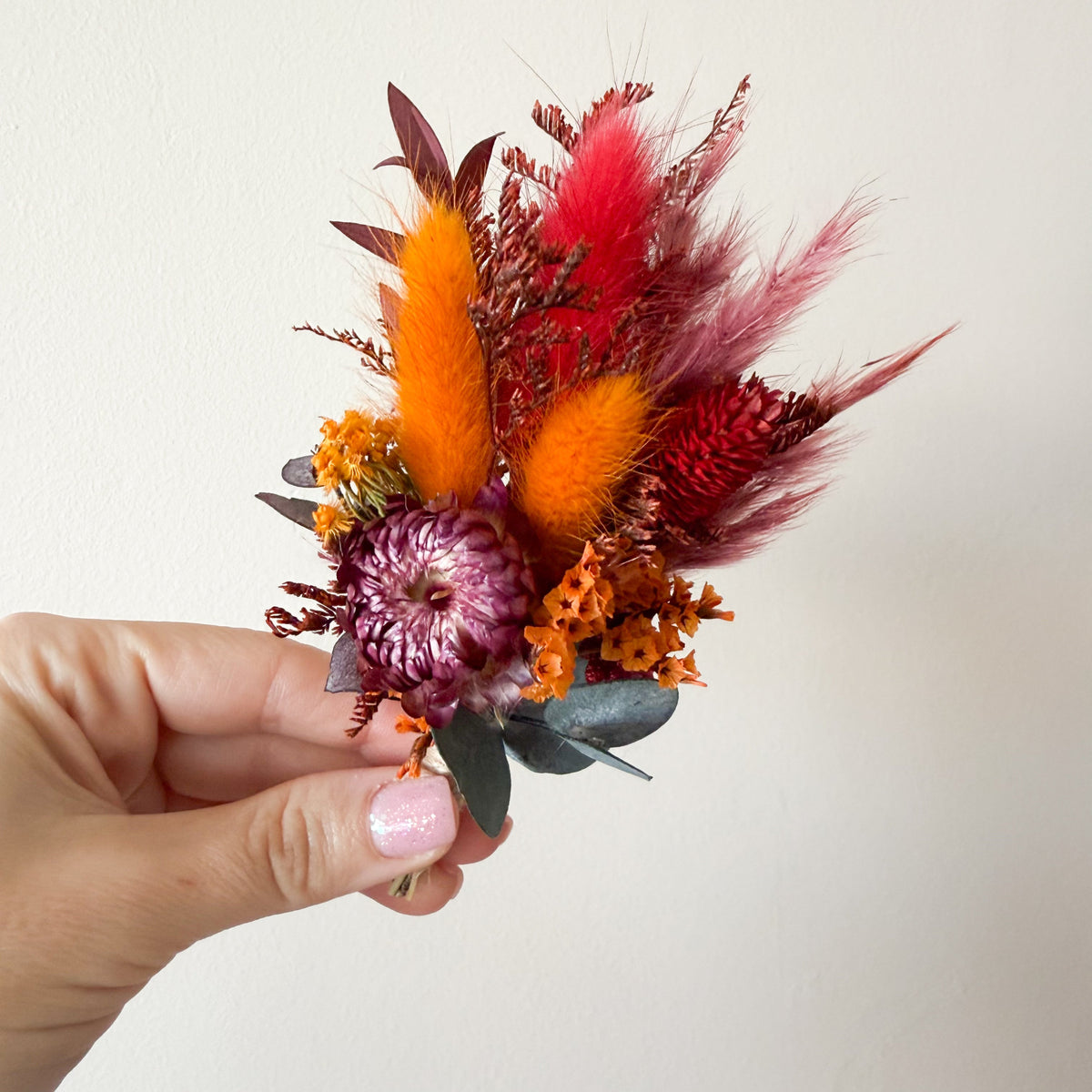 Burgundy and burnt orange dried flower wedding boutonniere with preserved flowers and eucalyptus foliage