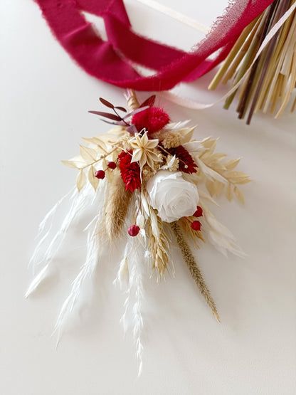 Close-up of boutonnière made from dried florals in ivory and burgundy, featuring sola rose, bunny tail grass, red accents and natural textures. Tied with deep red ribbon, designed for elegant Australian weddings with a timeless palette.