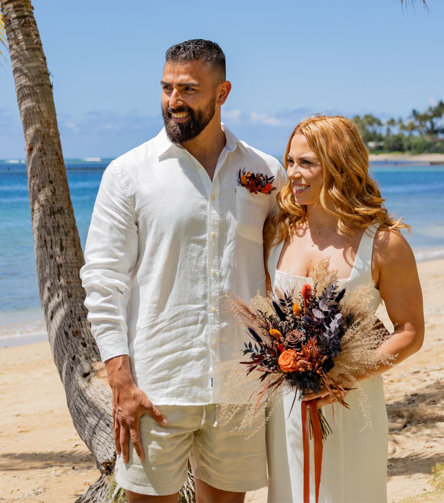 Bride and groom on a tropical beach with boho burnt orange and black dried flower wedding bouquet and matching boutonniere