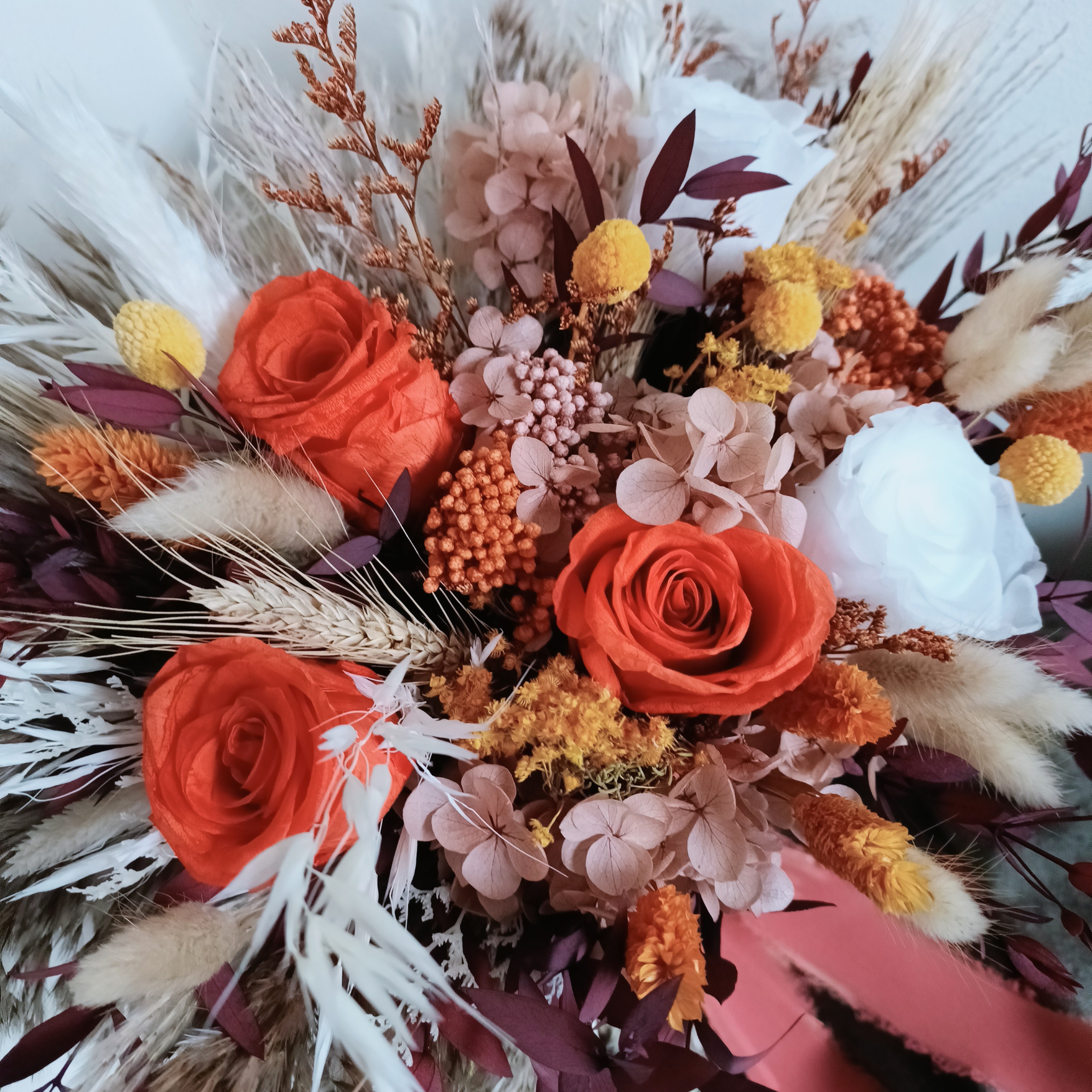 Close-up of dried wedding bouquet with orange sola roses, burgundy leaves, bunny tails, and soft ivory accents â€“ a textured, handcrafted arrangement perfect for autumn or terracotta-themed ceremonies.