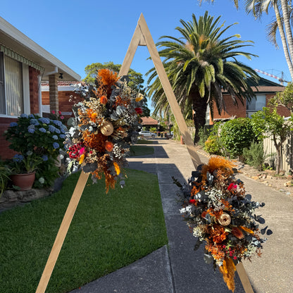 Decorative floral archway on a sidewalk with palm trees and houses in the background.