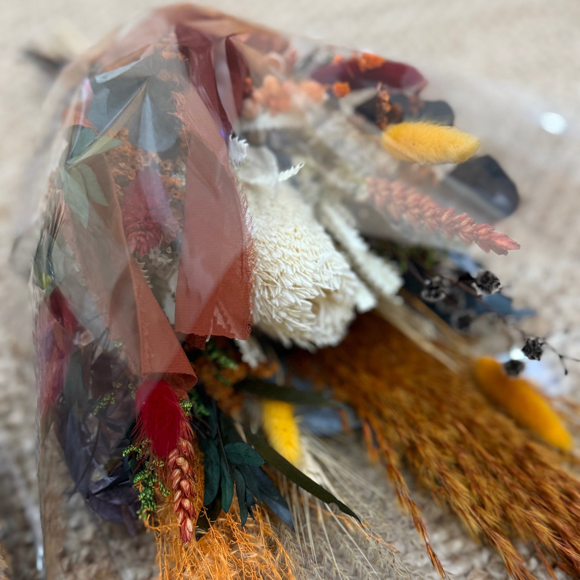 Dried flower bouquet in a clear plastic bag on a textured surface