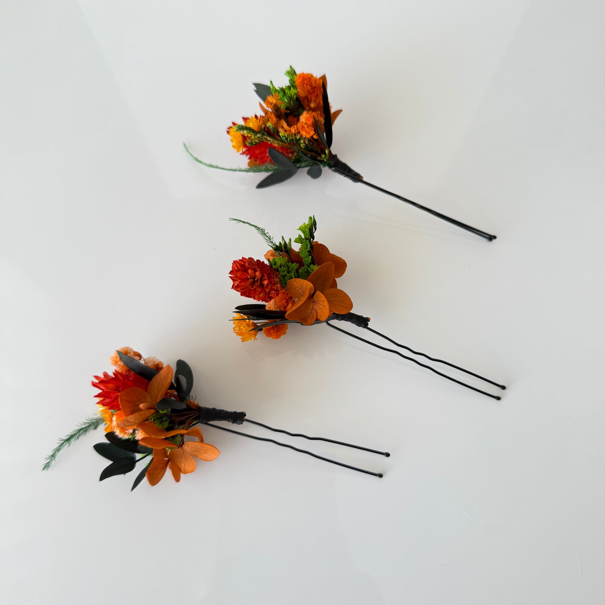 Three floral hairpins with orange and green flowers on a white background
