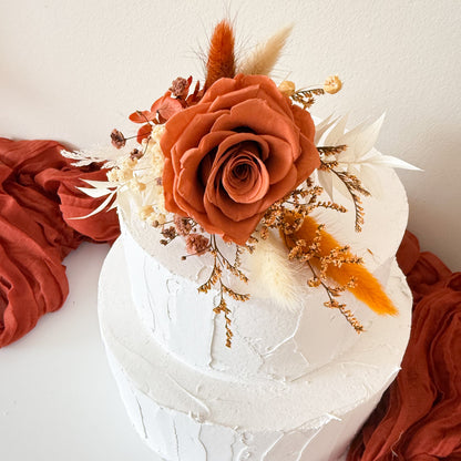 Close-up of burnt orange sola wood rose and preserved flowers used as rustic cake topper