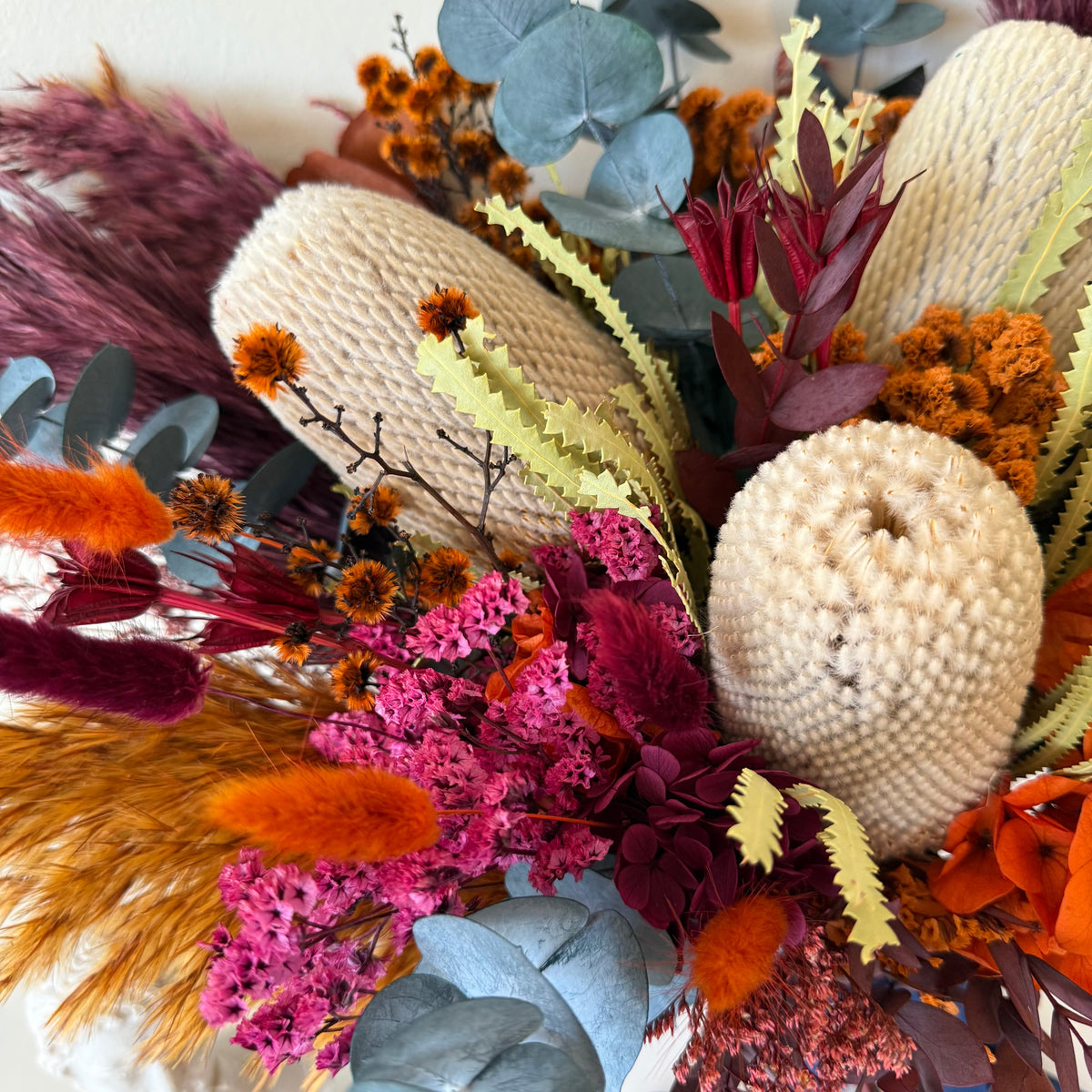 Close-up of preserved banksia surrounded by vibrant orange and pink dried flowers, burgundy foliage and blue eucalyptus.