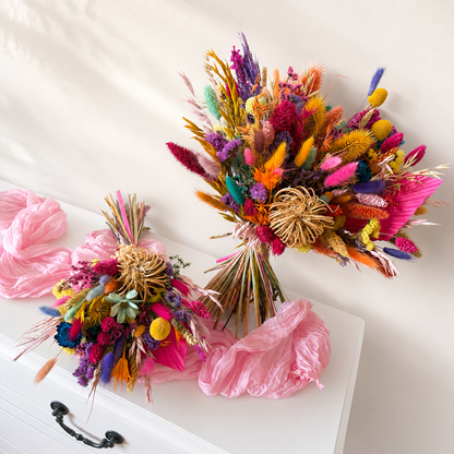 Colourful preserved flower wedding bouquet with matching bridesmaid bouquet arranged on soft pink fabric.