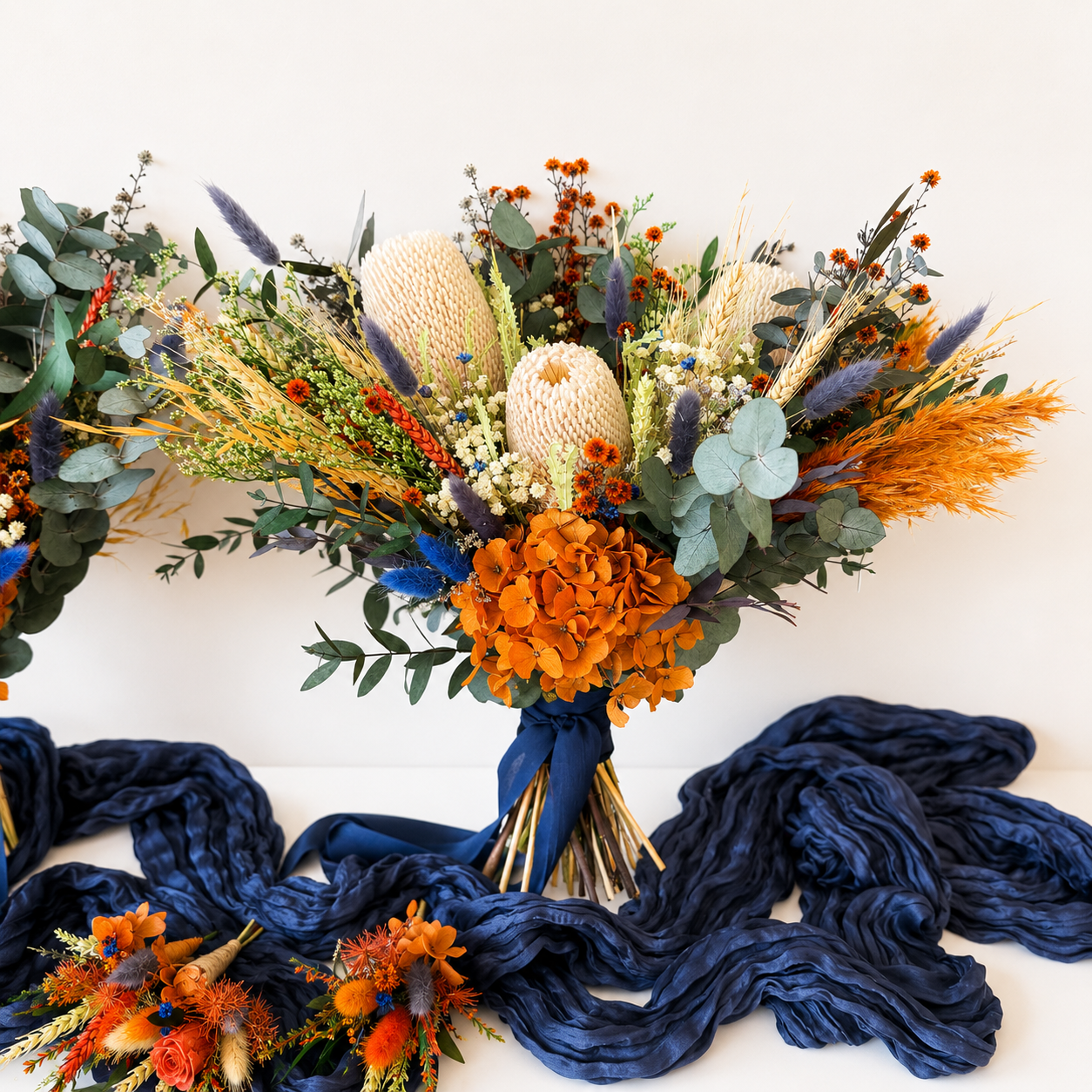 Complete Australian native wedding flower set including bridal bouquet, bridesmaid bouquet and matching dried wedding accessories in burnt orange and navy blue.
