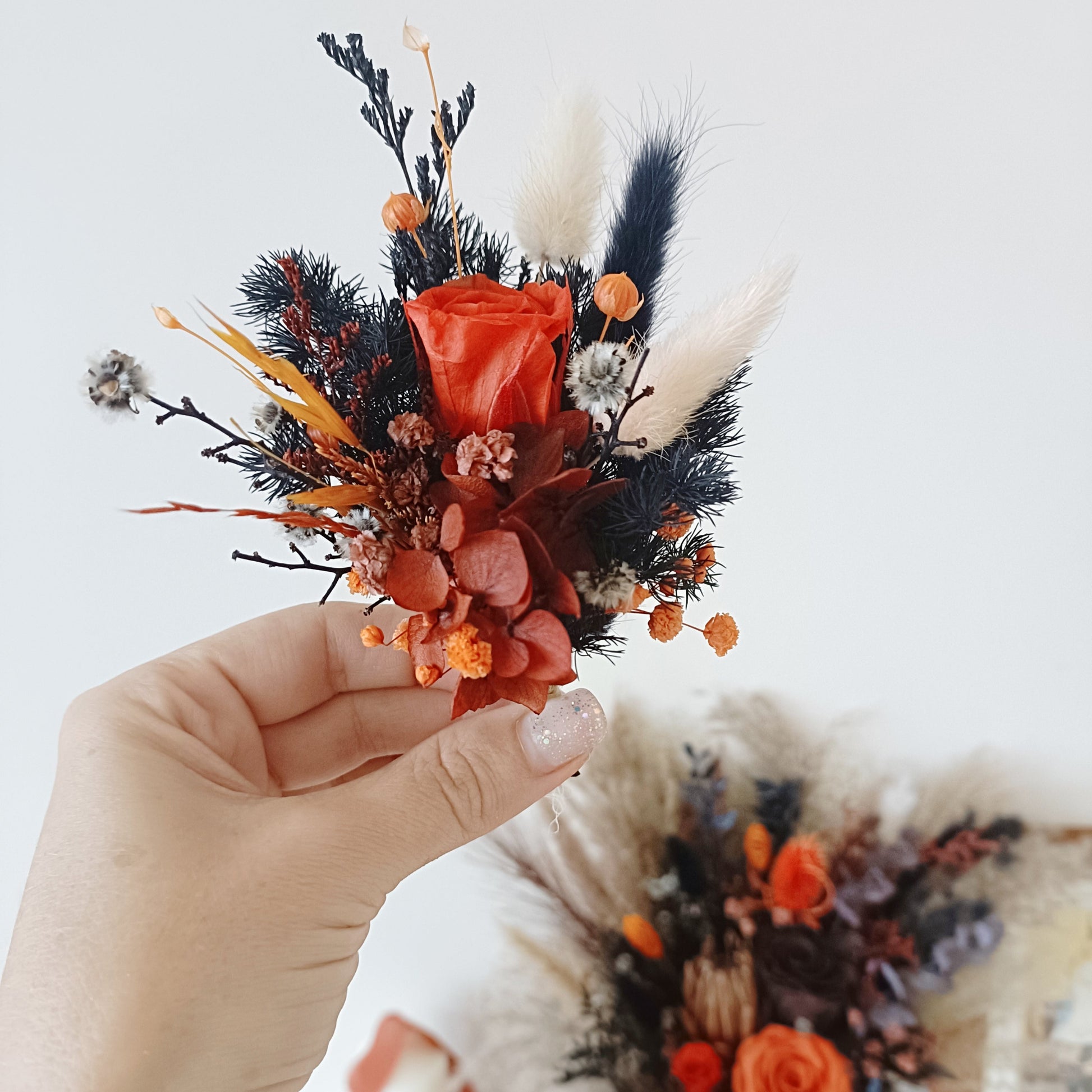nique dried floral groom pin with navy preserved leaves, orange blooms, and natural elements

