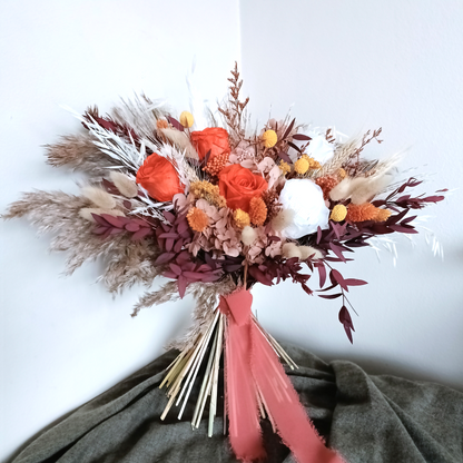 Front view of standing dried flower bouquet with burnt orange and white roses, craspedia, pampas grass, and burgundy foliage â€“ finished with long dusty pink ribbon.