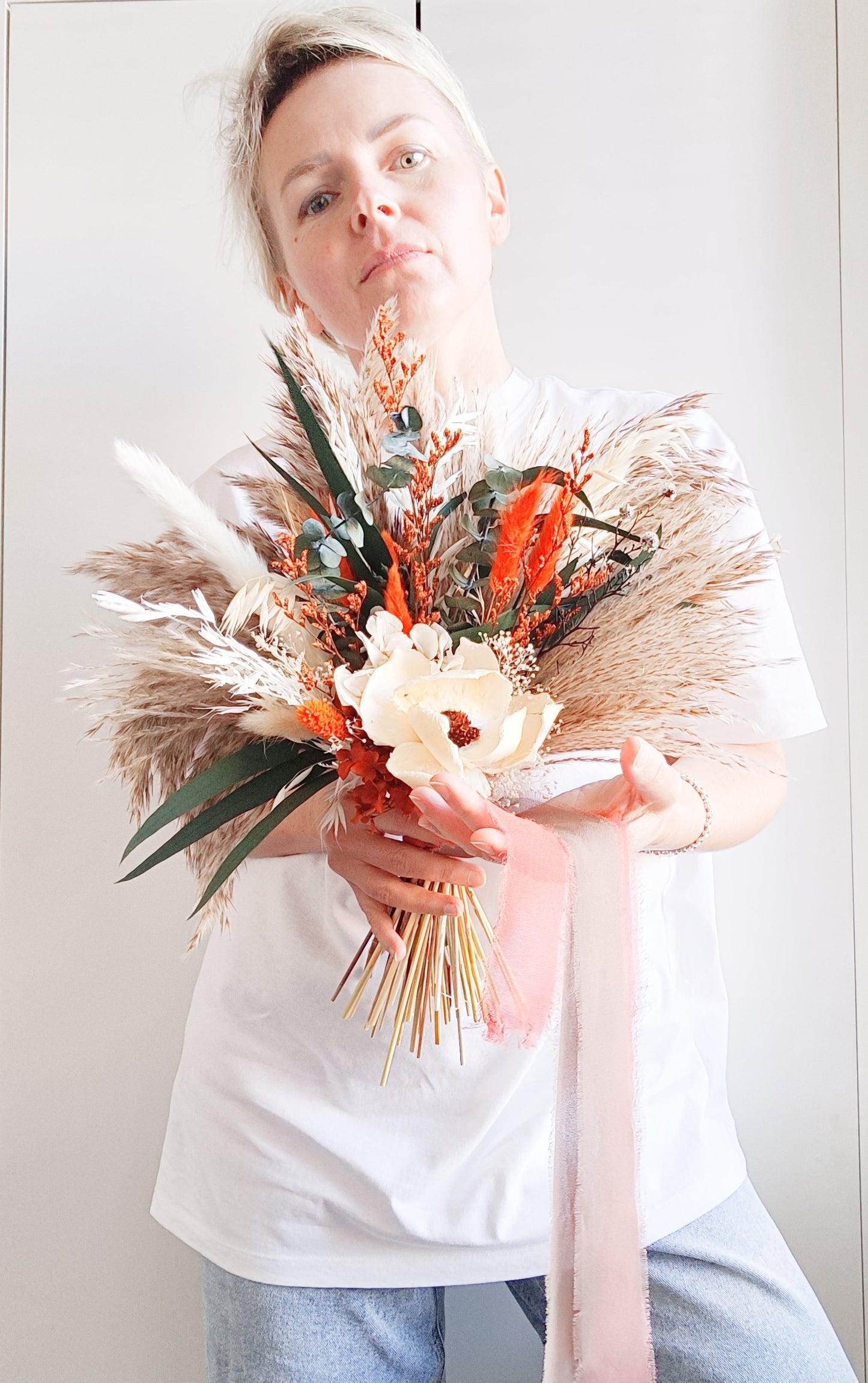 Close-up side view of preserved bouquet with orange flowers, sola blooms, dried greenery and pampas grass for natural, textured styling.