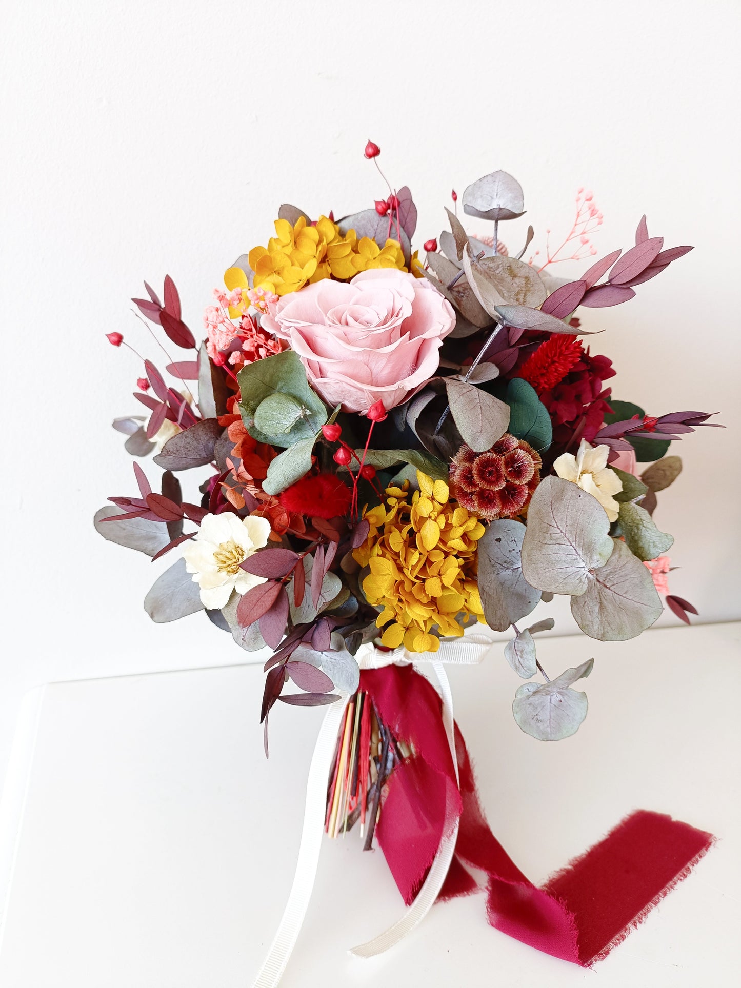 Romantic dried flower bouquet with preserved hydrangea, eucalyptus, ruscus, sola wood flowers and pink preserved roses, styled with velvet ribbon.