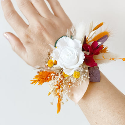 Close-up of dried flower wrist corsage in burgundy and ivory with sola wood rose