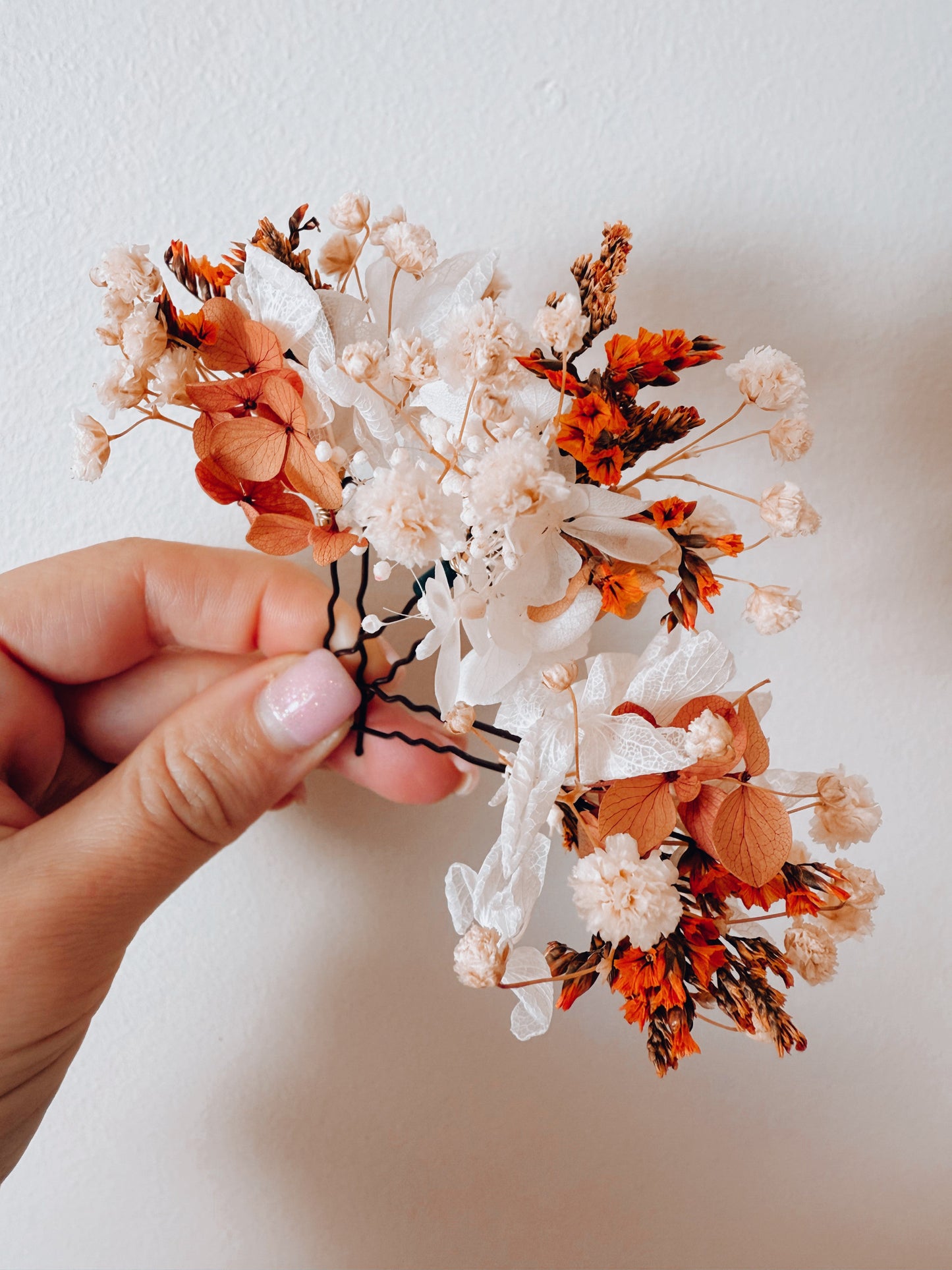 Hand-held dried flower bridal hairpiece in burnt orange and ivory tones, showing preserved flower details for boho and rustic brides