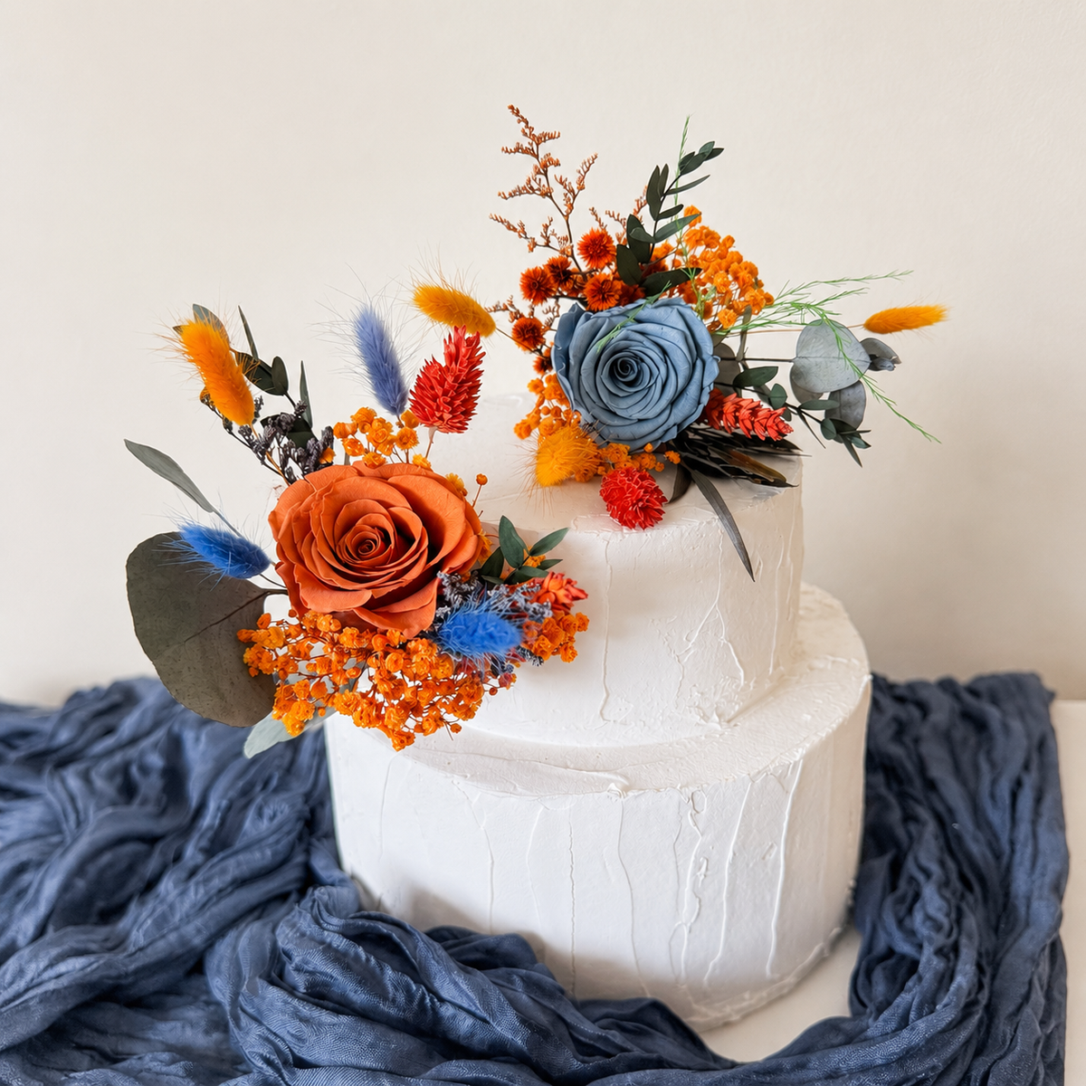 Natural dried and preserved cake topper arrangement featuring dusty blue roses, amber blooms and autumn foliage for a romantic boho wedding.