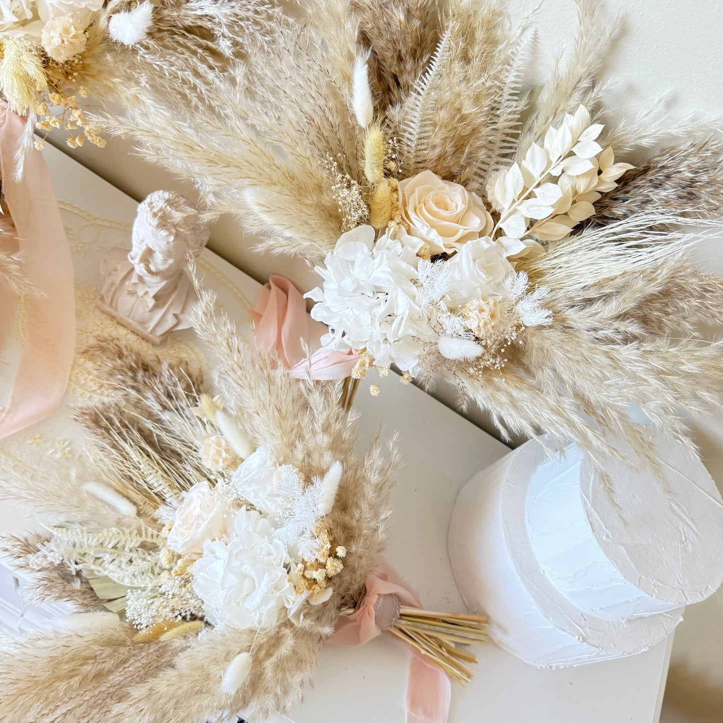Decorative floral arrangement with pampas grass and white flowers on a white surface.