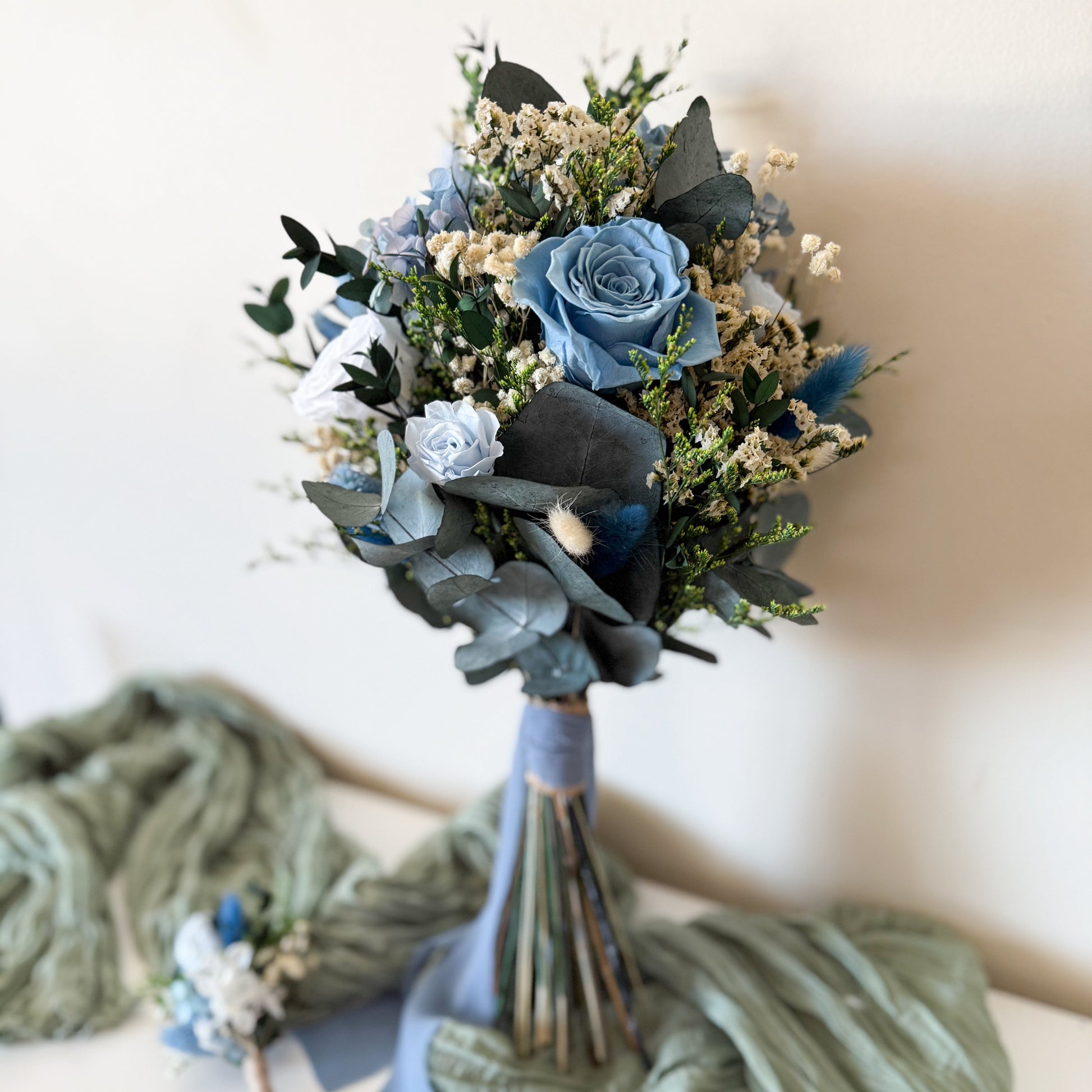 Handmade wedding bouquet in dusty blue and ivory tones with preserved greenery and sola wood flowers, ideal for brides.