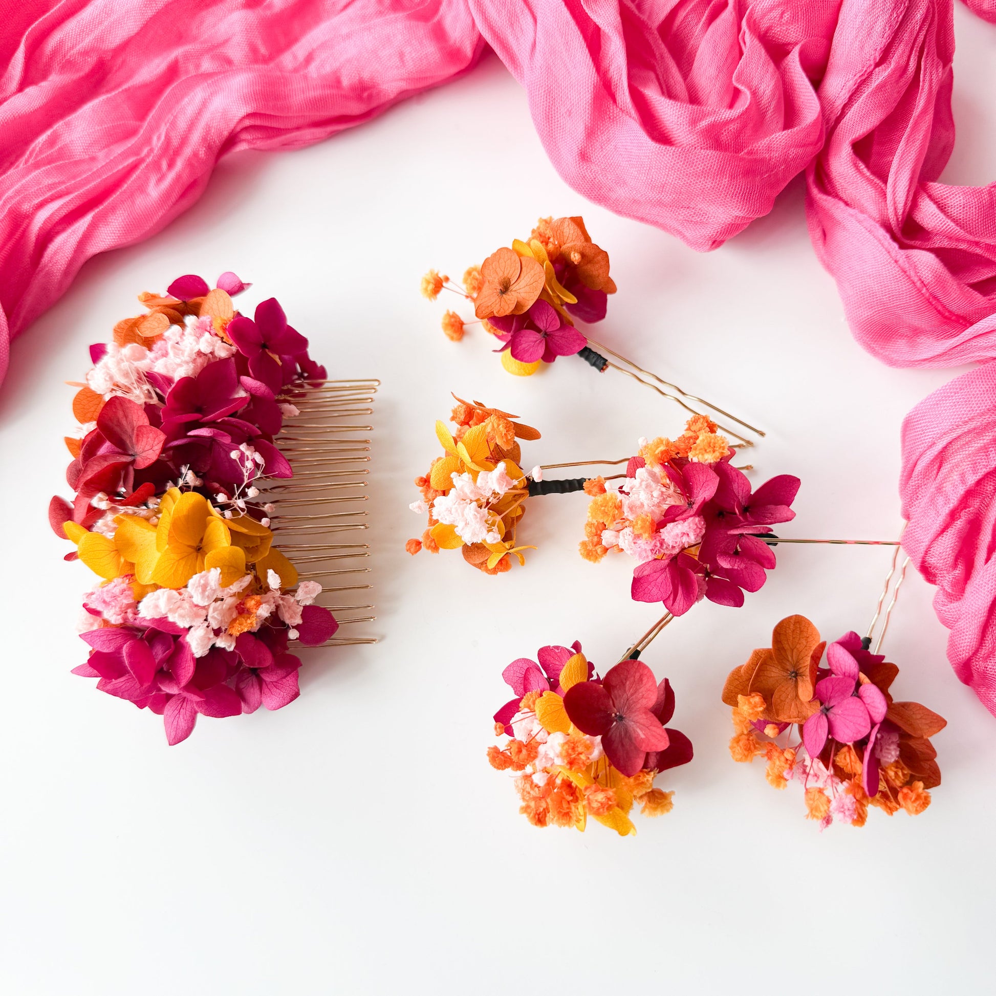 Colorful floral hair accessories on a white surface with pink fabric.